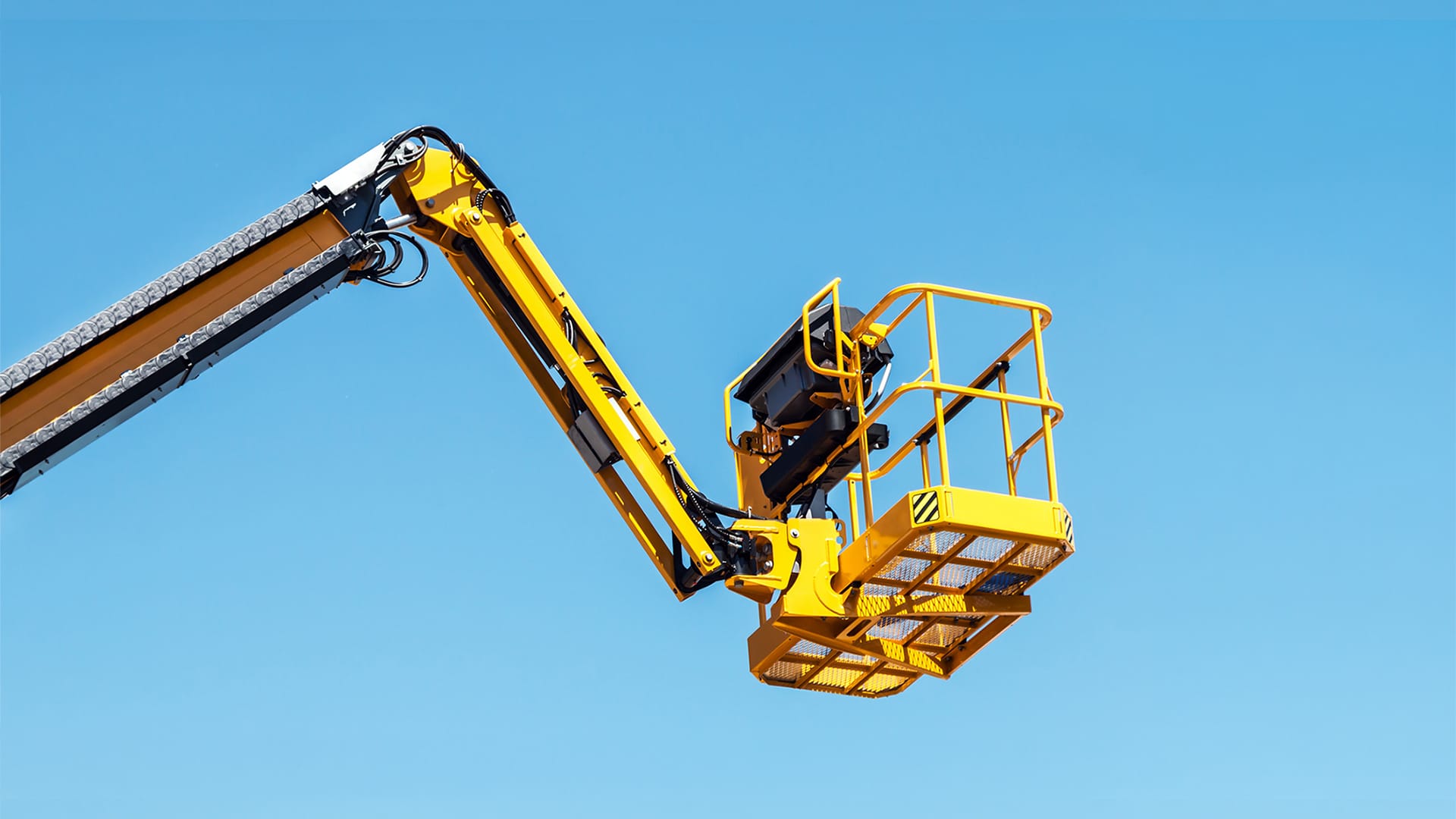 Courses > IPAF 3a and 3b > Header > Background Yellow mobile elevating work platform with an extended boom against a clear blue sky.