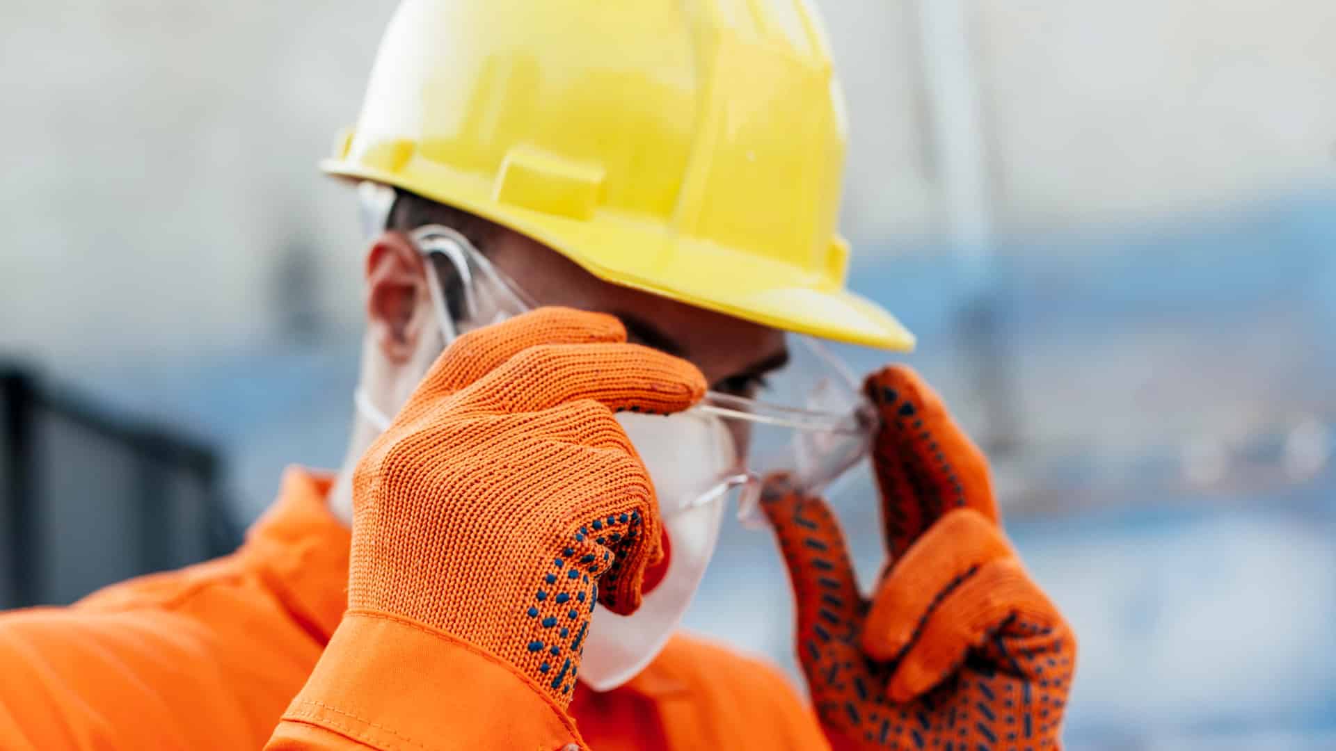 Courses > NEBOSH > Header > Background Construction worker wearing a yellow hard hat, safety glasses, face mask and protective gloves.