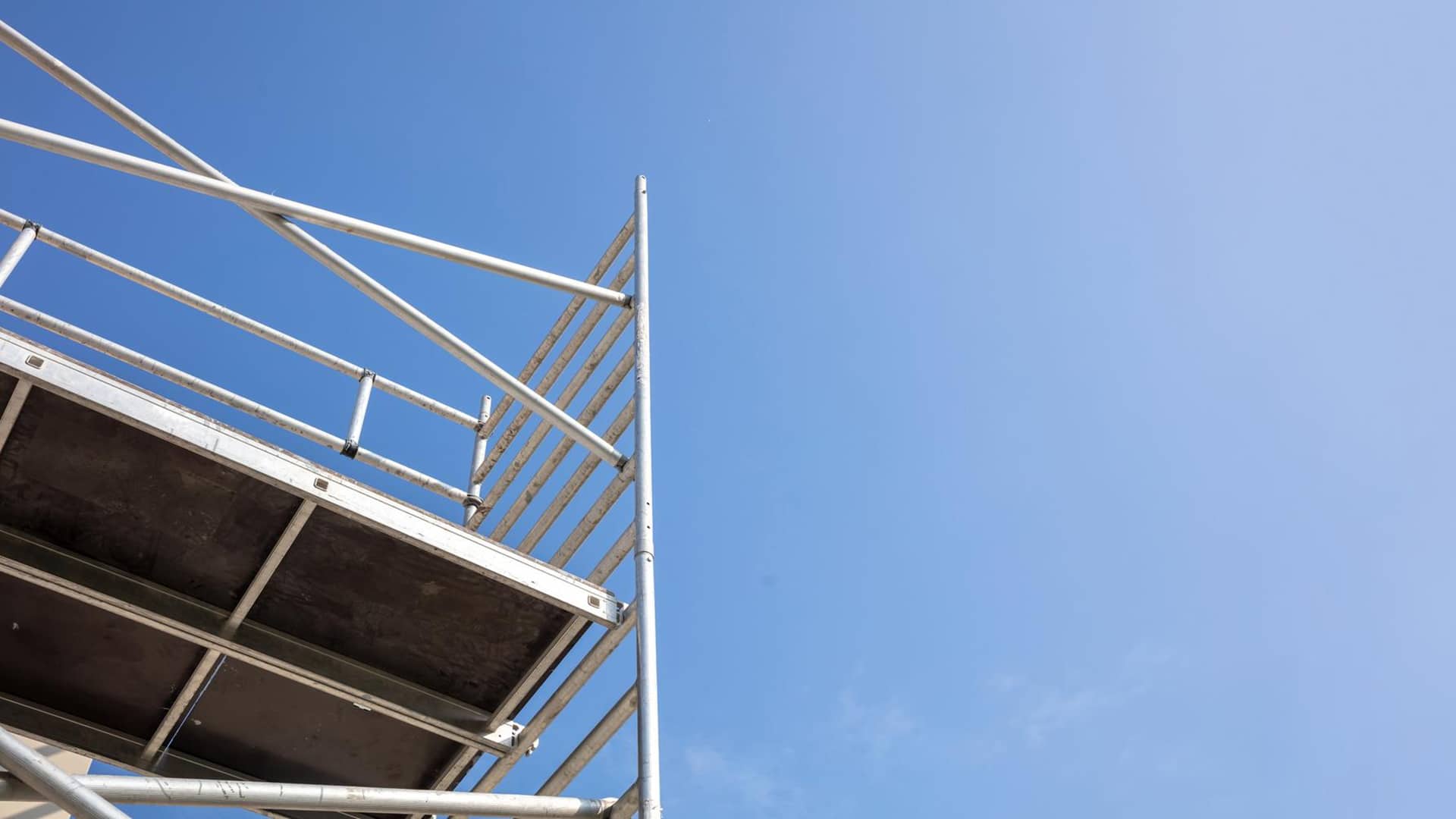 Courses > PASMA Towers for Users > Header > Background Metal scaffold tower viewed from below against a clear blue sky.