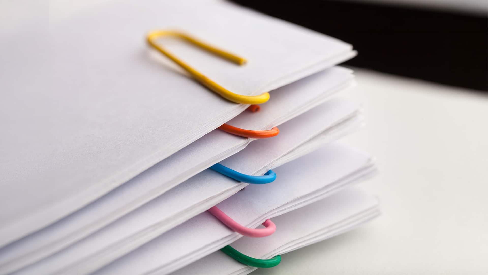 Resources > Case Studies > Header > Background Stack of documents organised with colourful paper clips.