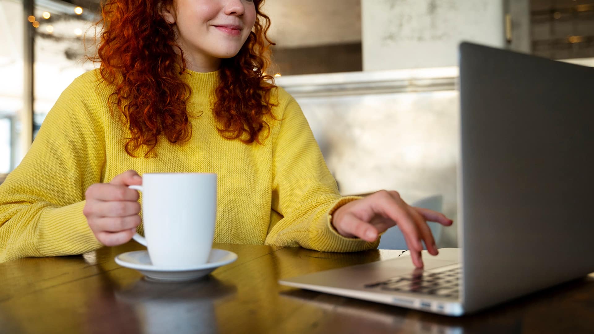 Your LMS > Header > Background Woman using a laptop while holding a cup of coffee, representing flexible online learning.