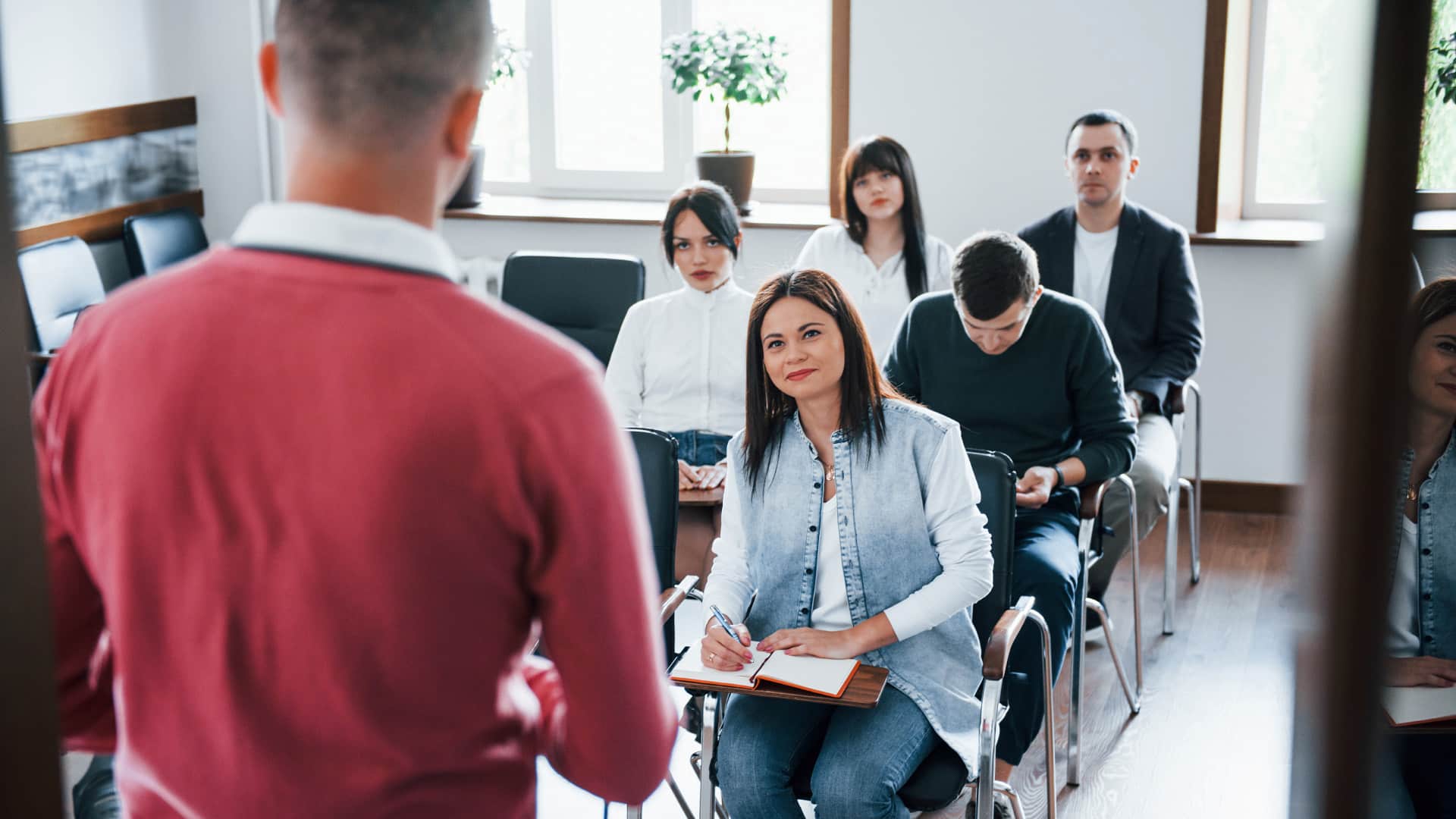 Courses > Header > Background Trainer presenting to a group of adult learners in a classroom, with attendees taking notes.